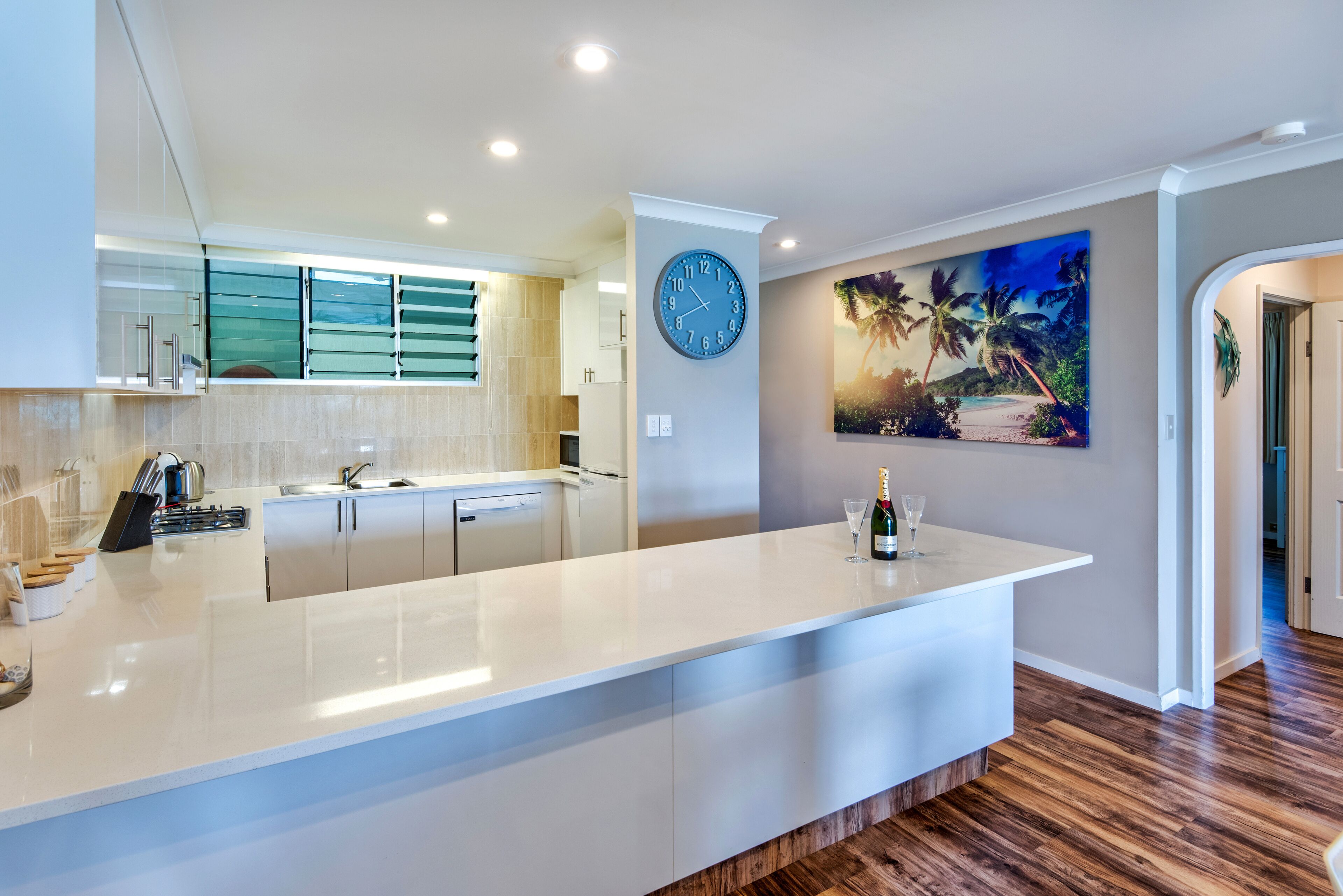 Een moderne keuken met een wit aanrecht, een klok en een schilderij van een strand.