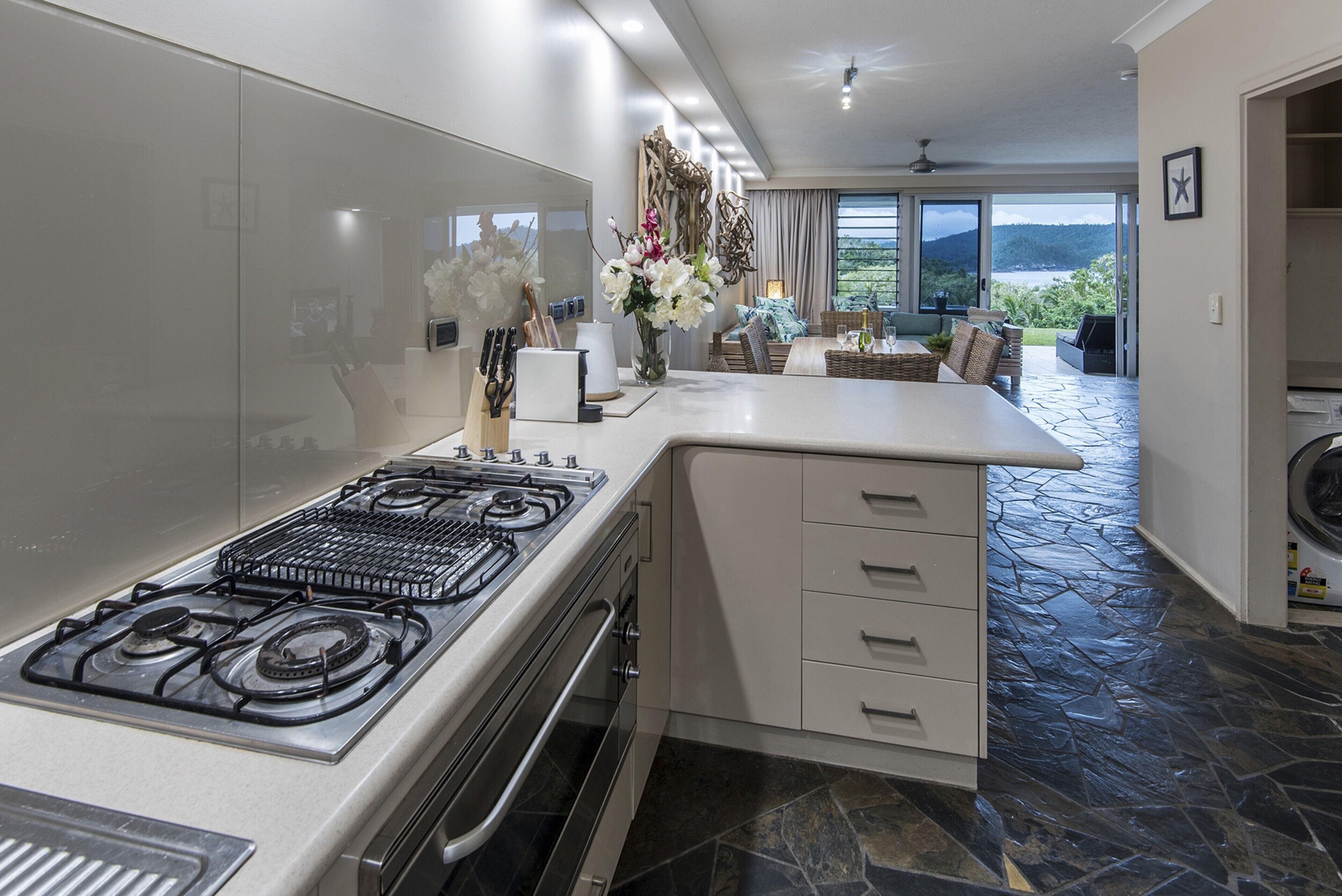 Une cuisine moderne dotée d’une cuisinière à gaz, de meubles blancs et d’un sol en pierre.