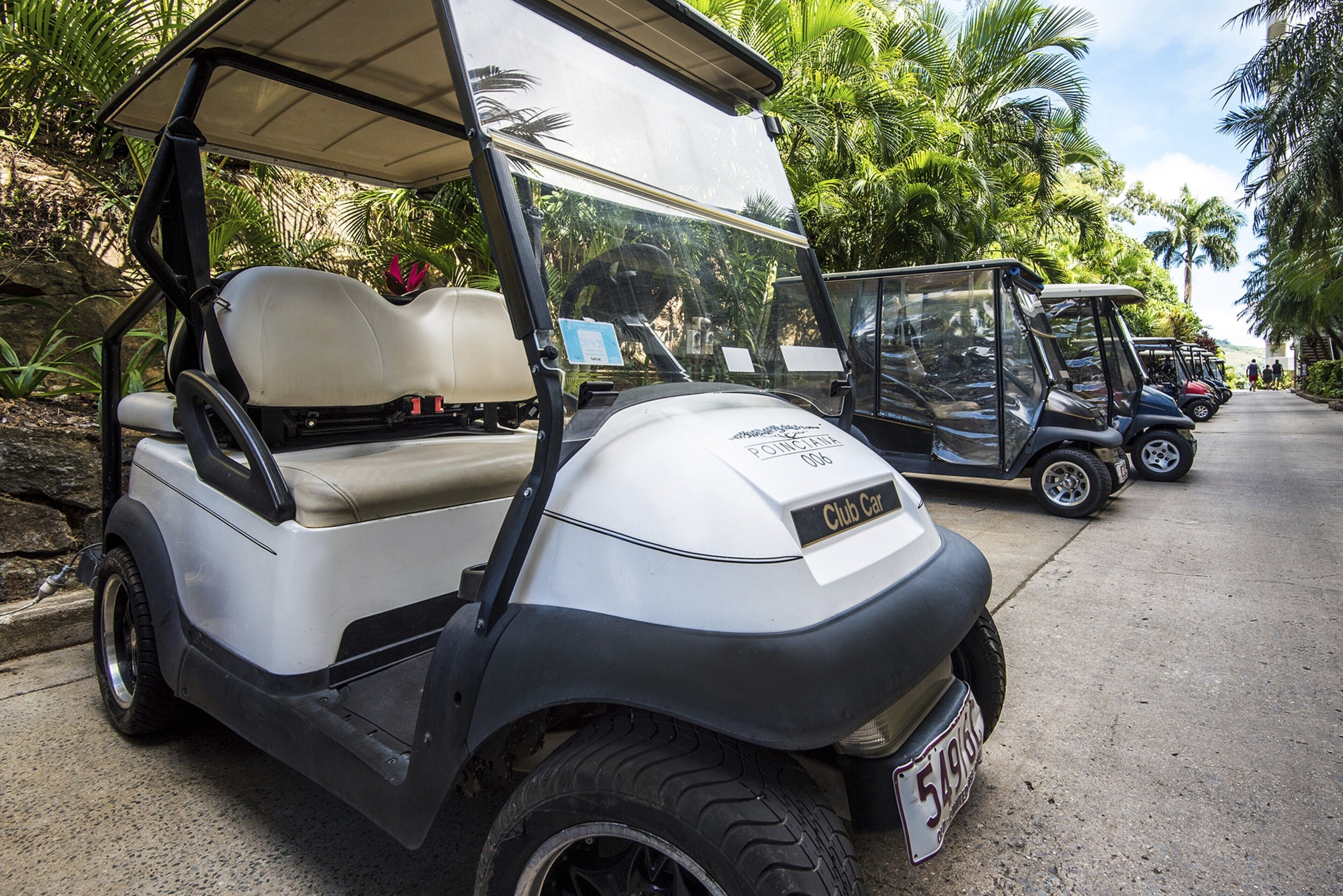 A golf cart parked on a street with palm trees and a building in the background.