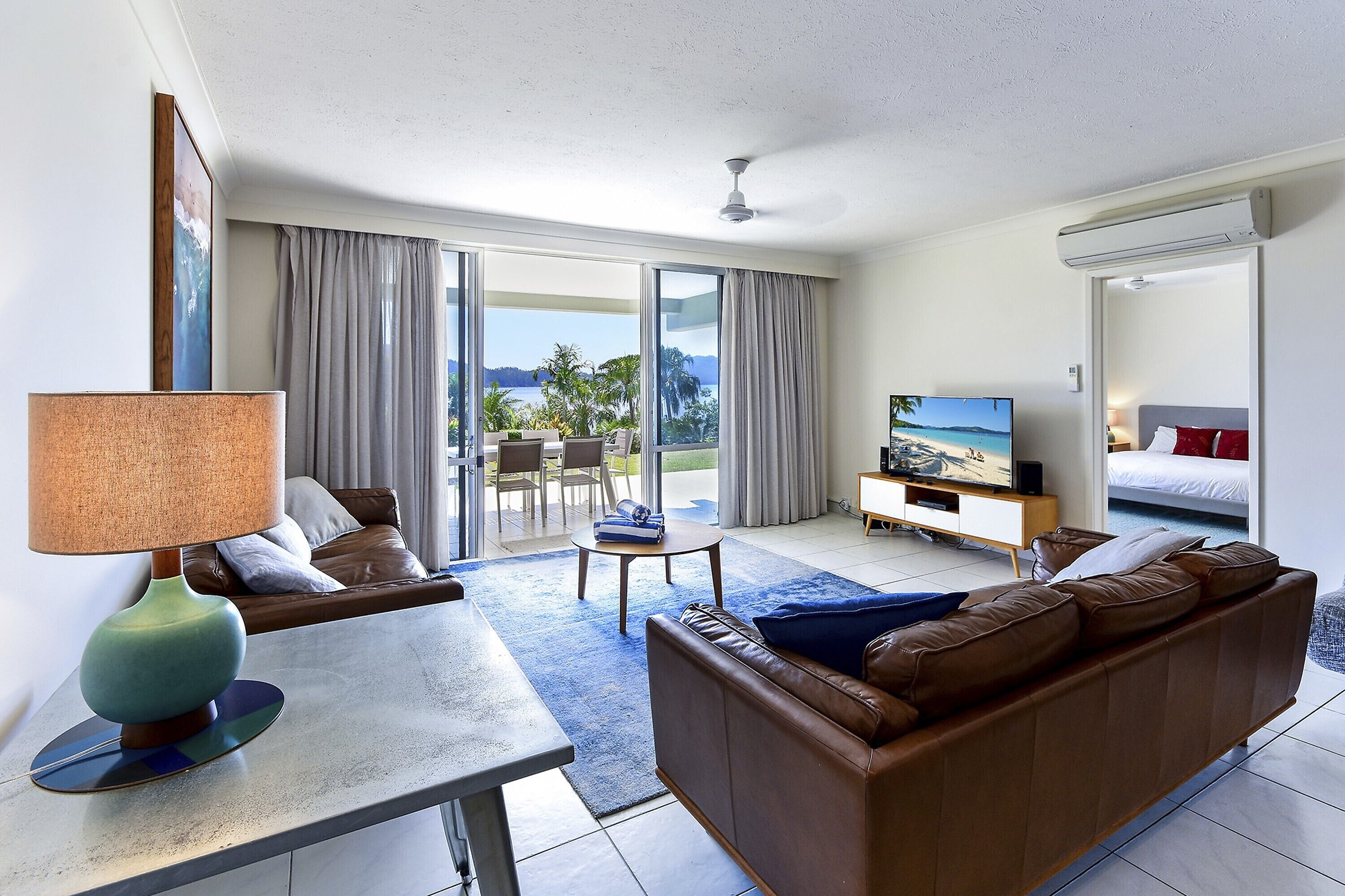 A modern hotel room with a sofa, a TV, a dining table, and a view of the outdoors.