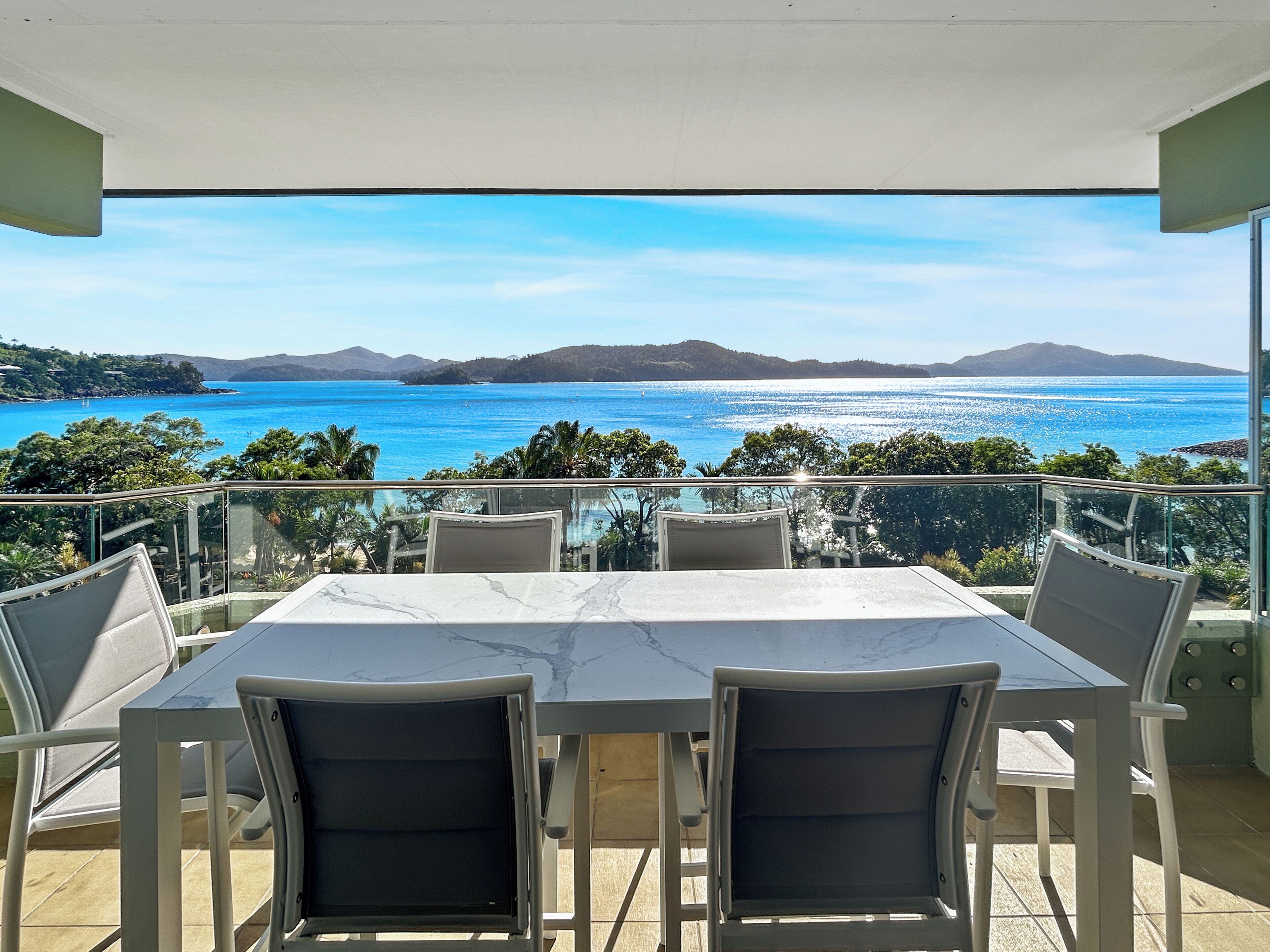 A terrace with a table and chairs, overlooking a scenic view of the sea and distant mountains.