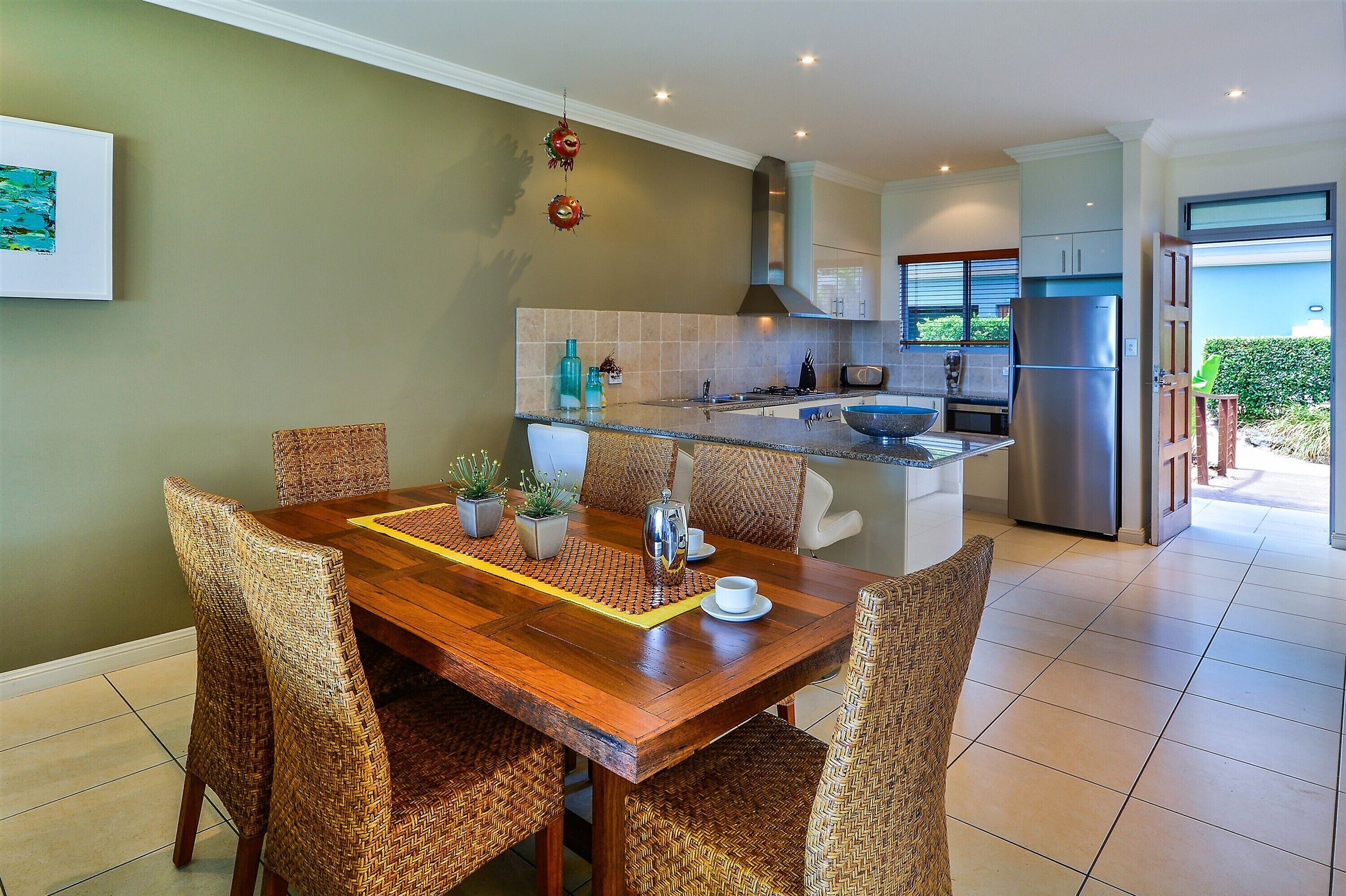 A modern kitchen with a wooden dining table, wicker chairs, and a view to the outside.