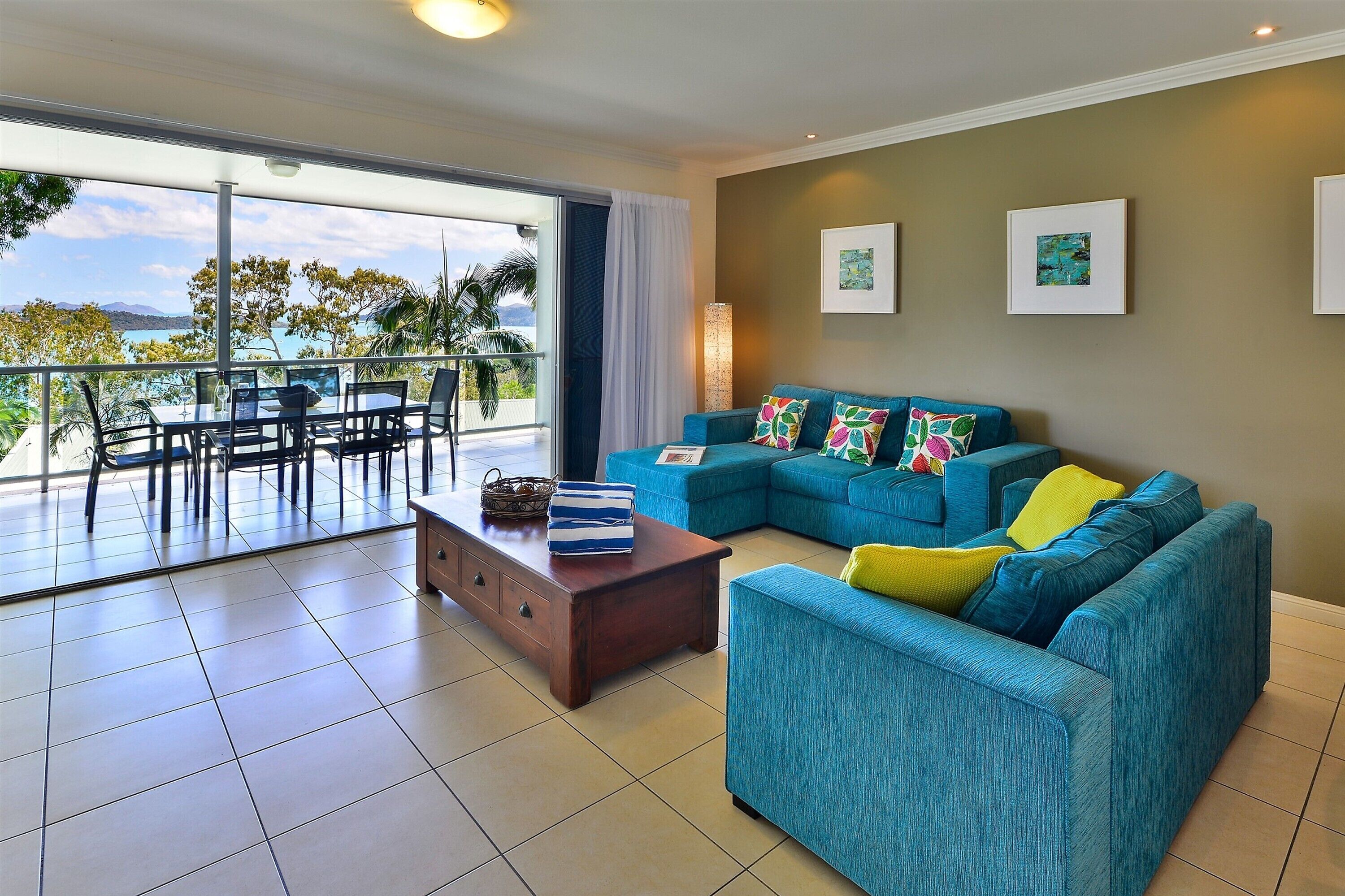A living room with a blue sofa, a wooden coffee table, and a balcony with a view of the sea.
