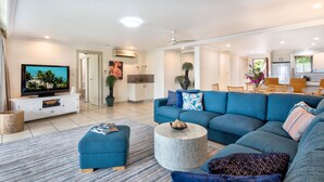 Un salon moderne avec un grand canapé, un pouf et un téléviseur à écran plat posé sur un meuble de télévision blanc.