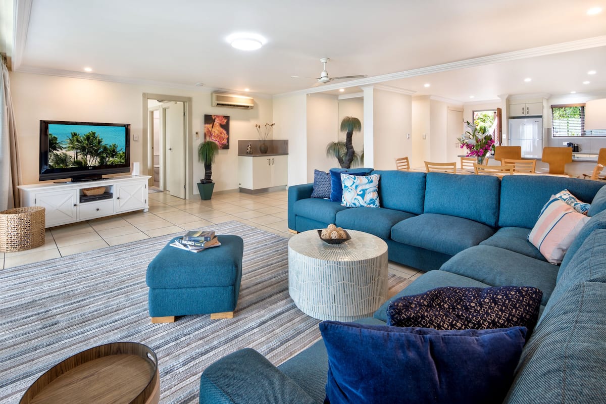 A modern living room with a large sofa, ottoman, and a flat-screen TV on a white entertainment unit.