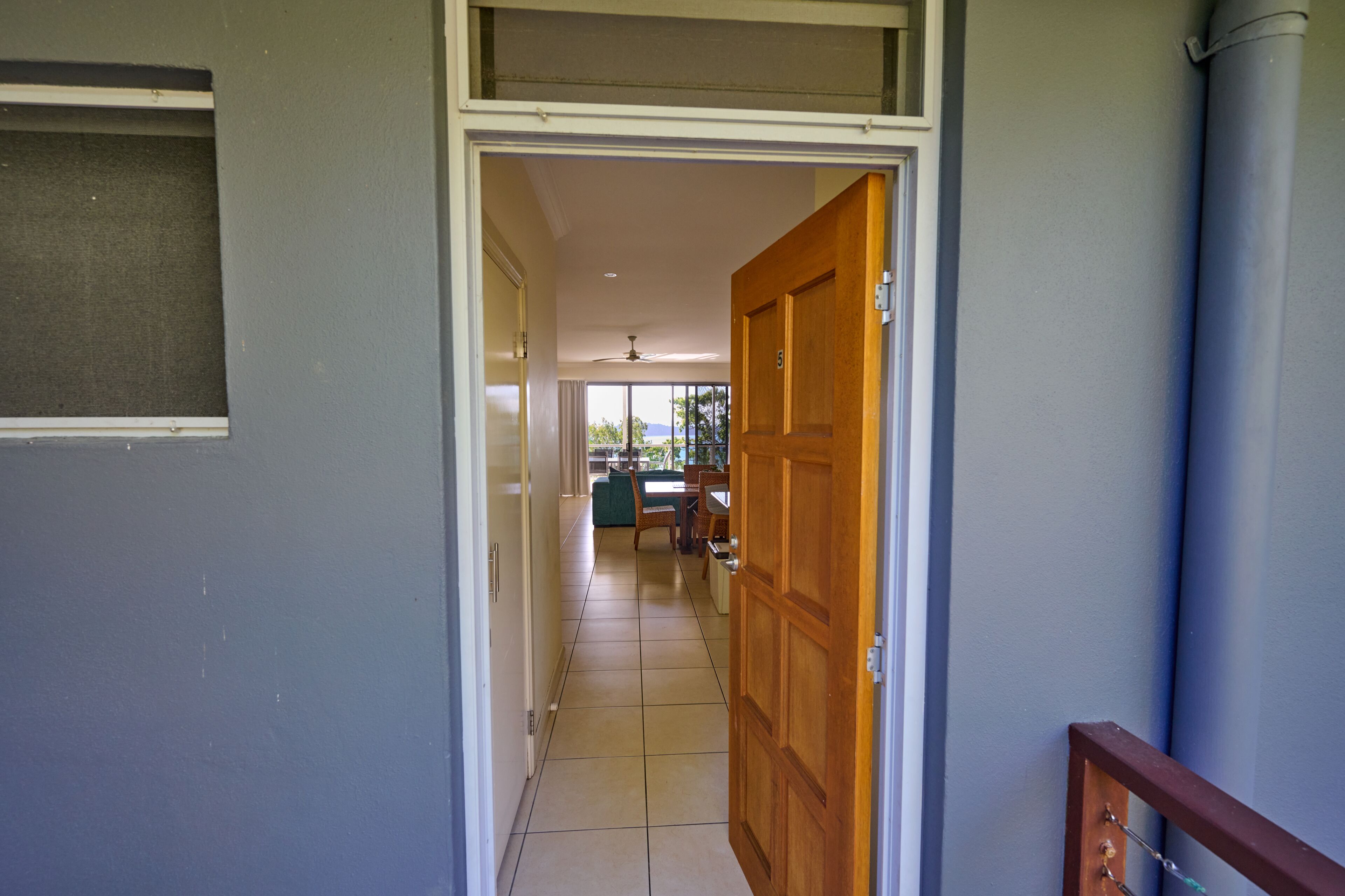 A hallway leading to a dining area with a ceiling fan, a wooden door, and a view of the outdoors.
