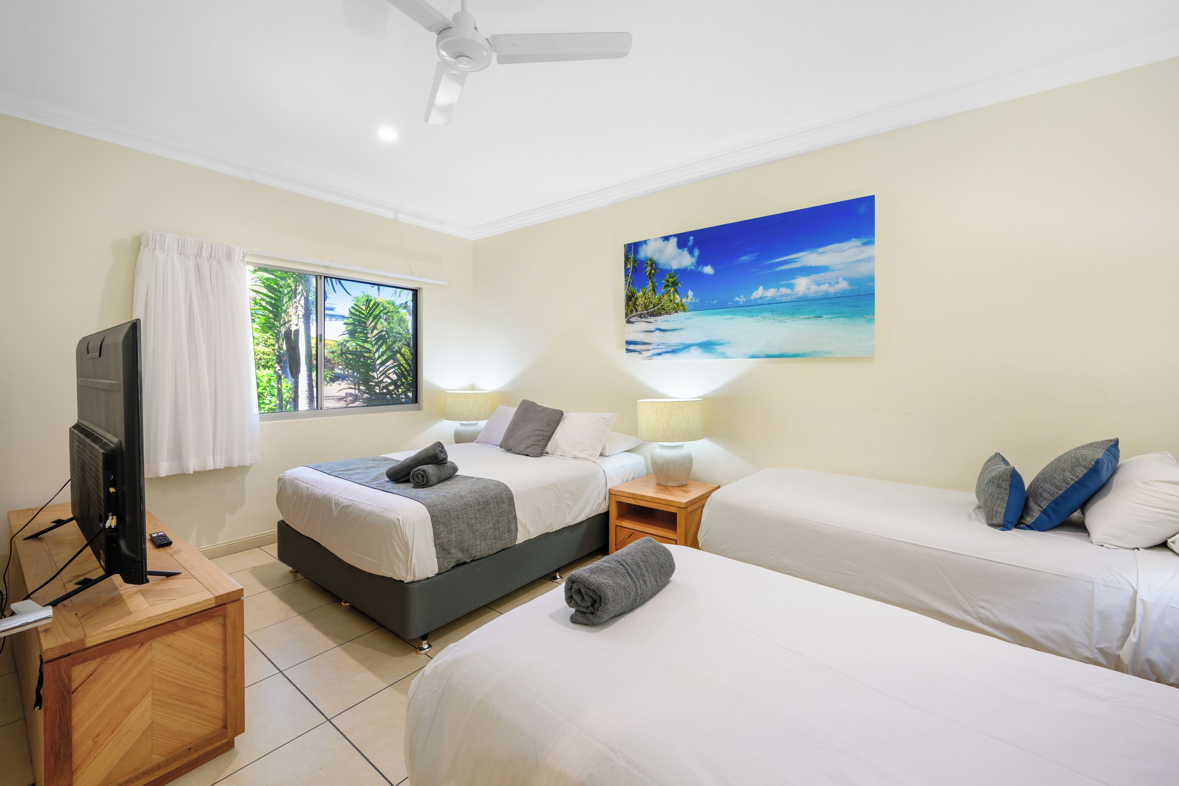 A hotel room with two beds, a television, a desk, and a painting of a beach scene.