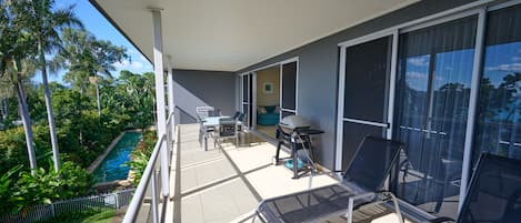 Een balkon met een zwembad, buitenmeubels en uitzicht op het omliggende groen.