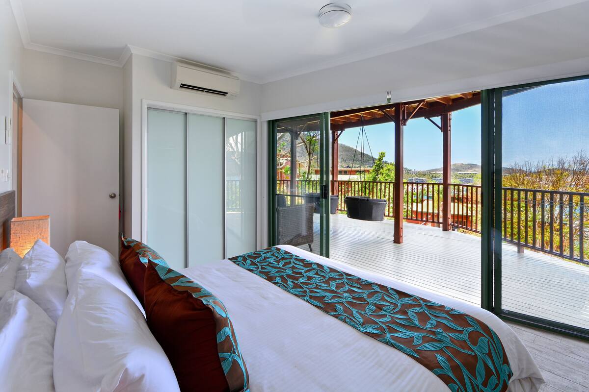 A hotel room with a bed, a sliding glass door leading to a balcony with a view of the landscape.