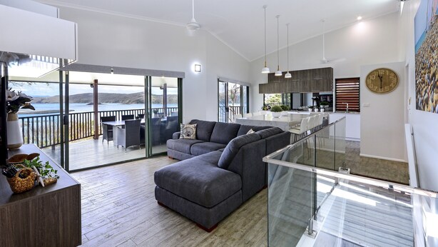 Un salon moderne avec un canapé d’angle, une balustrade en verre et une vue sur l’extérieur.