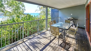 A balcony with a table and chairs, overlooking a scenic view of the sea and greenery. - Heliconia Grove 9 (Whitsundays)