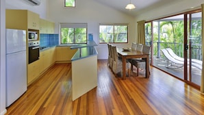 A modern kitchen with a central island, wooden flooring, and large windows offering views of greenery. - Heliconia Grove 9 (Whitsundays)