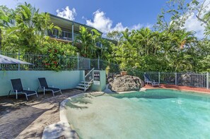 A pool area with lounge chairs, a staircase leading to a balcony, and lush tropical vegetation. - Heliconia Grove 9 (Whitsundays)