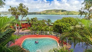 A pool surrounded by lush greenery and a view of a lake and hills. - Heliconia Grove 9 (Whitsundays)