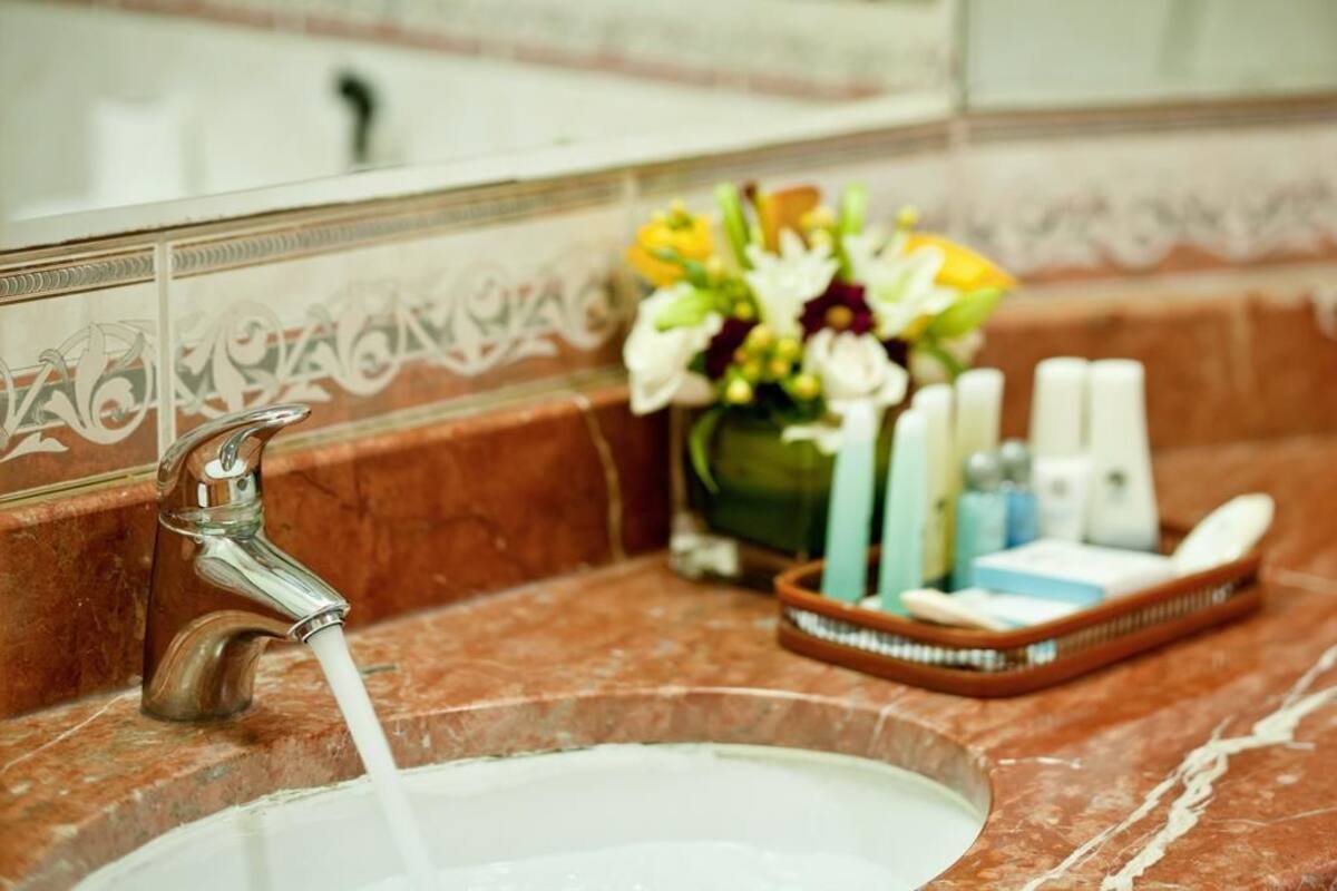 A bathroom sink with running water, a vase of flowers, and toiletries on the counter.