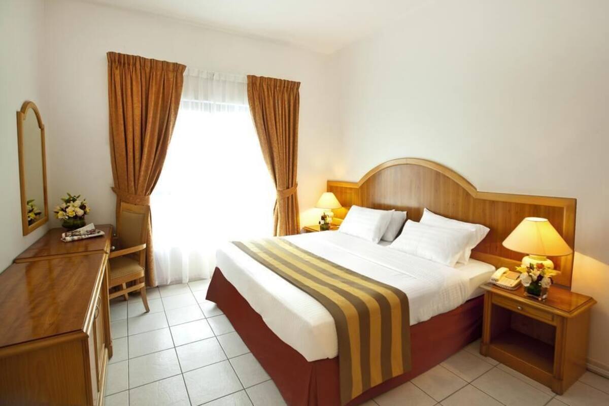 A hotel room with a bed, bedside tables, a desk, a chair, and a window with curtains.