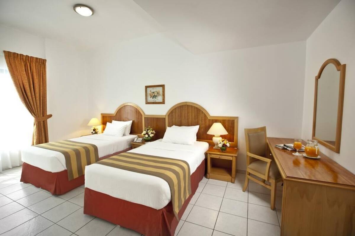 A hotel room with two beds, a desk, a chair, a mirror, and a picture on the wall.