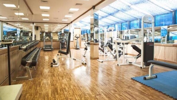 A gym with wooden flooring, various exercise equipment, and large windows allowing natural light. - Dock Masters Hotel Apartments (Dubai)