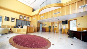A hotel lobby with a reception desk, a large red carpet, and a high ceiling with a glass railing. - Dock Masters Hotel Apartments (Dubai)
