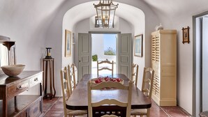 A dining area with a wooden table, chairs, a chandelier, and a view through an open door. - Nautilus (Santorini)