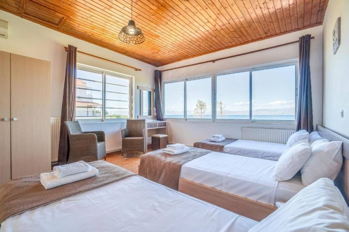 Ein Hotelzimmer mit zwei Betten, einem Sessel, einem Schreibtisch und einem großen Fenster mit Blick auf das Meer.