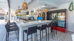 Een moderne bar met een centraal eiland, zwarte barkrukken en een gekoelde displaykast.