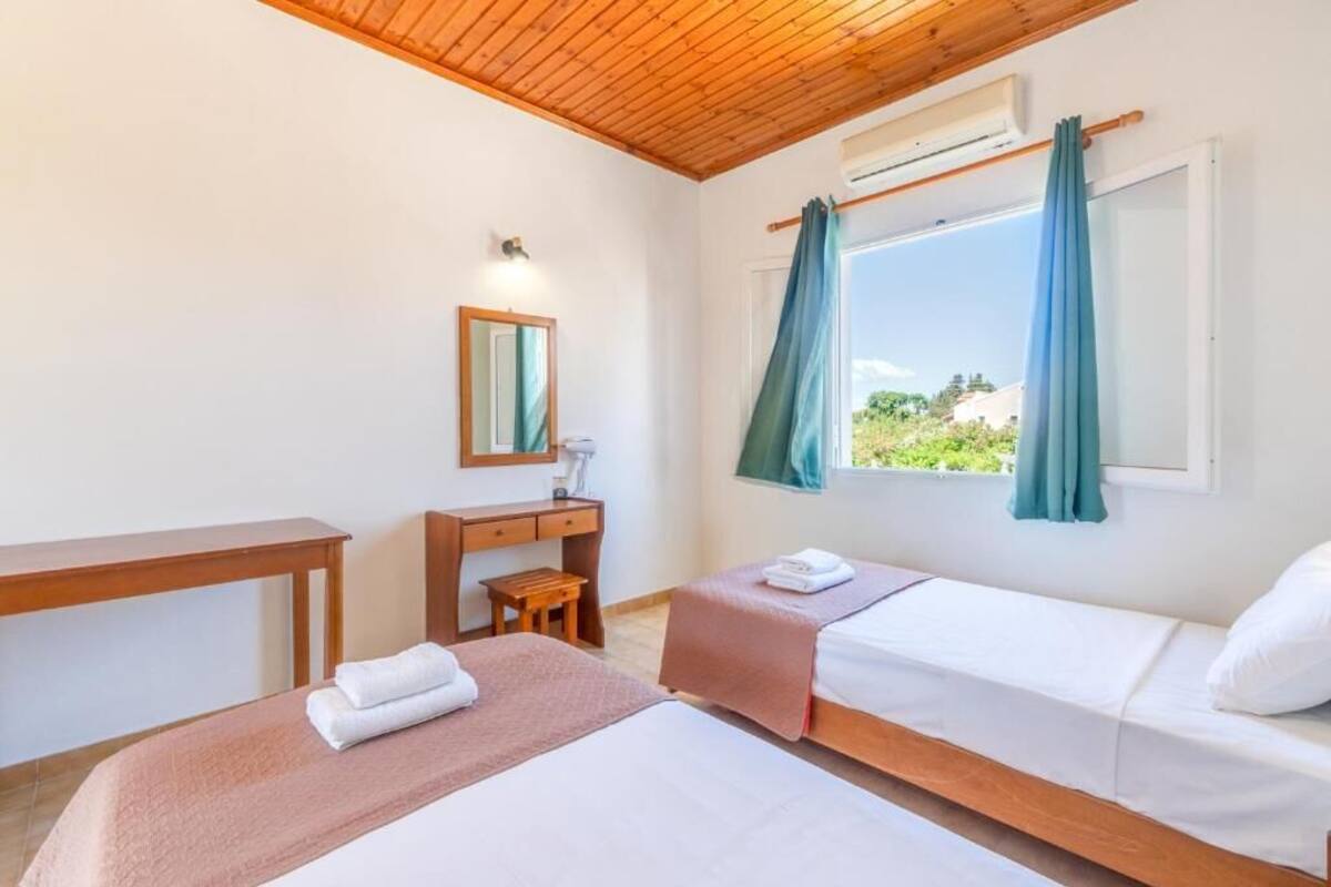 Ein Zimmer mit zwei Betten, einem Schreibtisch, einem Stuhl, einem Spiegel und einem Fenster mit Vorhängen.