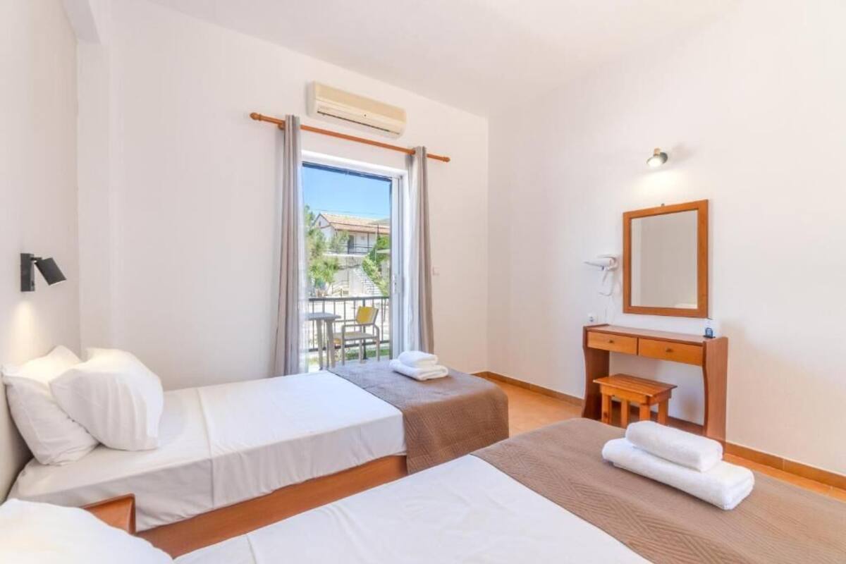 Ein Hotelzimmer mit zwei Betten, einem Holztisch, einem Spiegel und einem Fenster mit Vorhängen.
