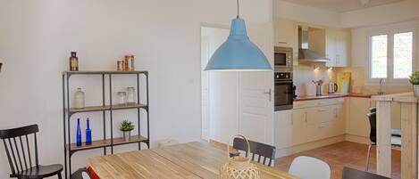 A modern kitchen with white cabinets, a blue pendant light, and a dining area with a wooden table and chairs.