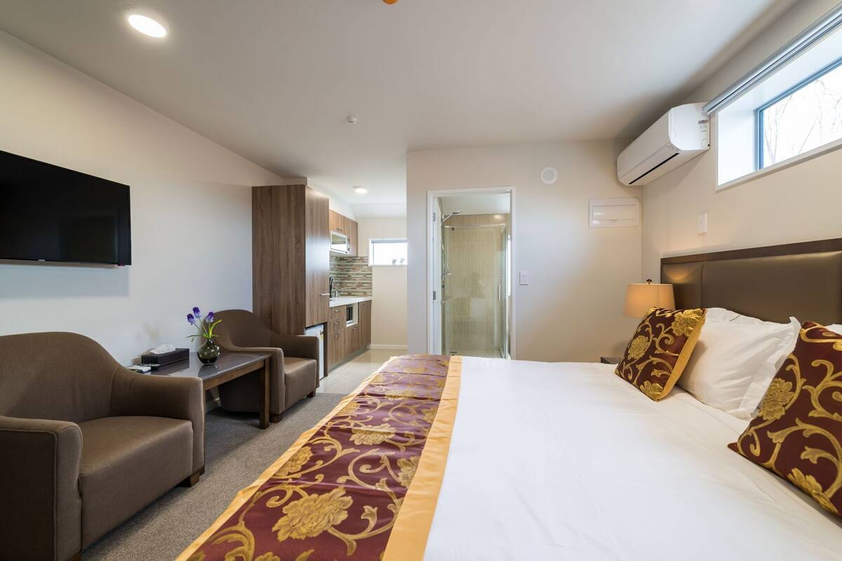 A hotel room with a bed, a desk, a chair, a TV, and a bathroom door.