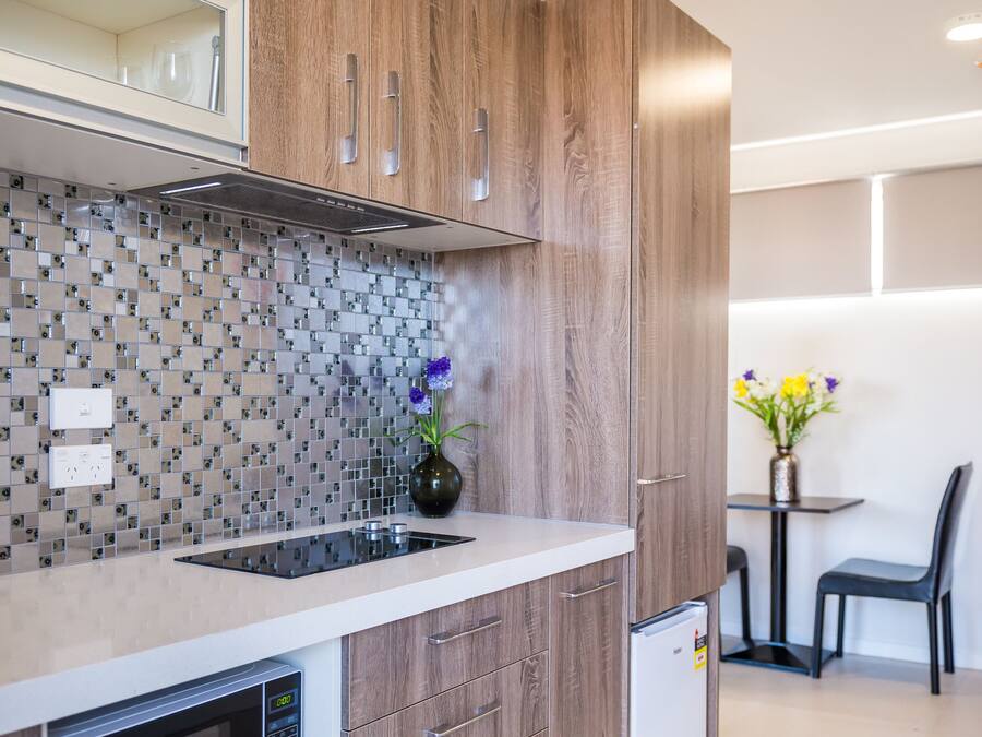 A modern kitchen with wooden cabinets, a built-in microwave, and a tiled backsplash.