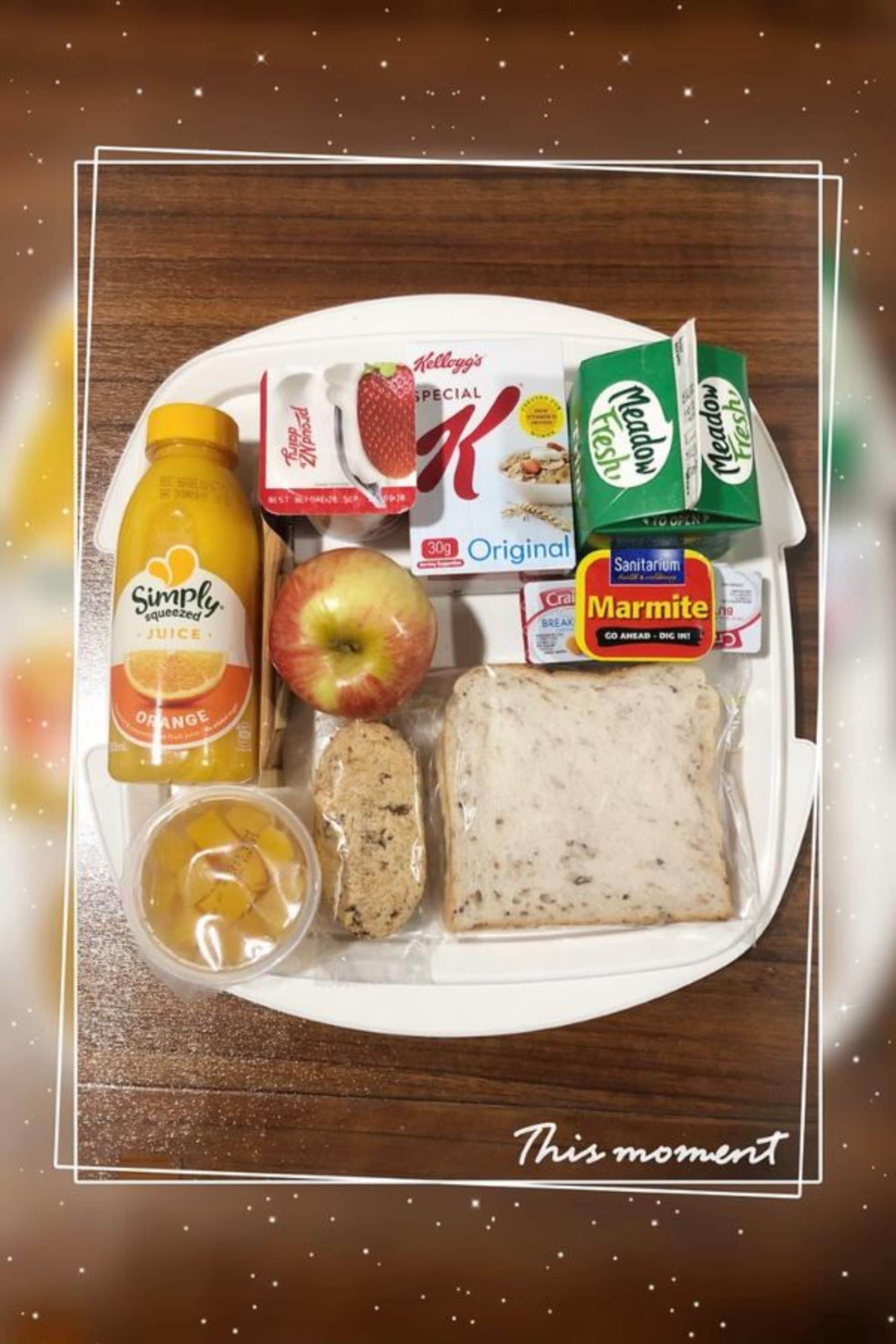 A meal tray with a bottle of orange juice, an apple, a loaf of bread, a box of Marmite, a carton of milk, a box of Kellogg's Special K, and a box of Meadow Fresh milk.