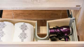 Un armario de madera con dos toallas blancas de diseños intrincados y un secador de pelo morado.
