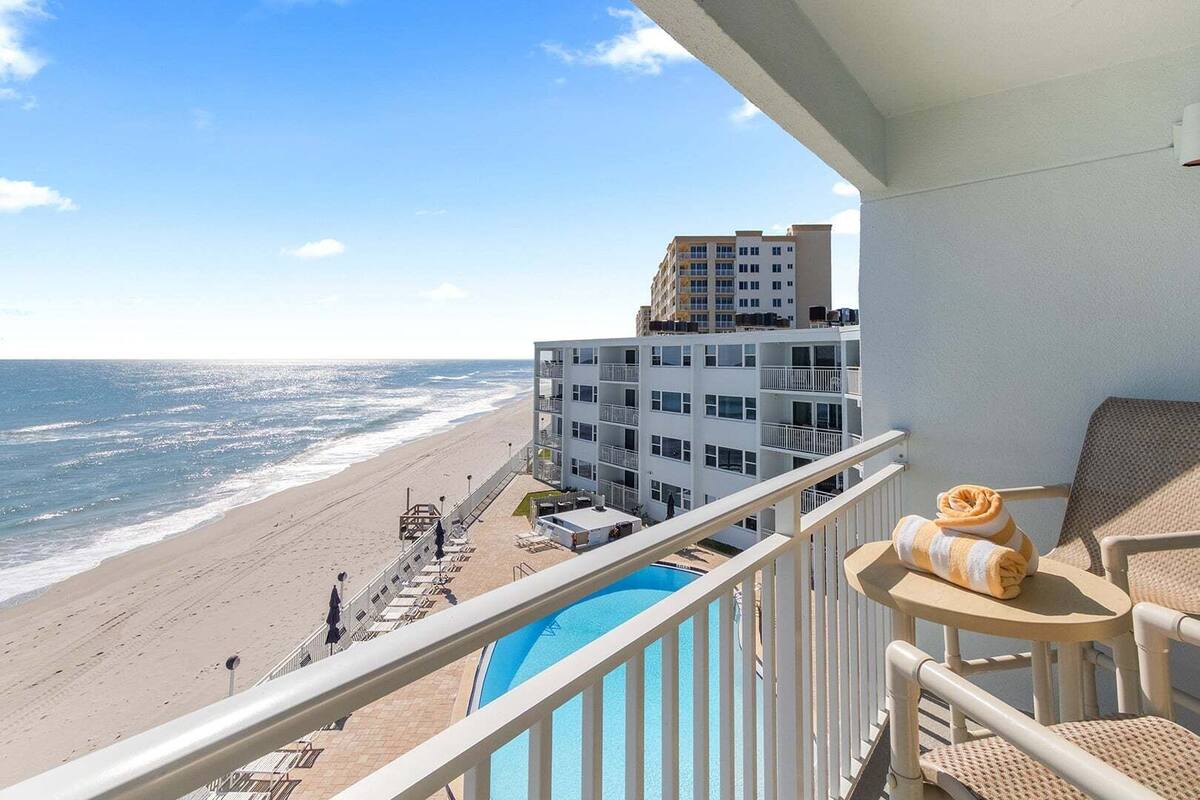 A balcony with a pool, beach view, and a building with multiple floors.