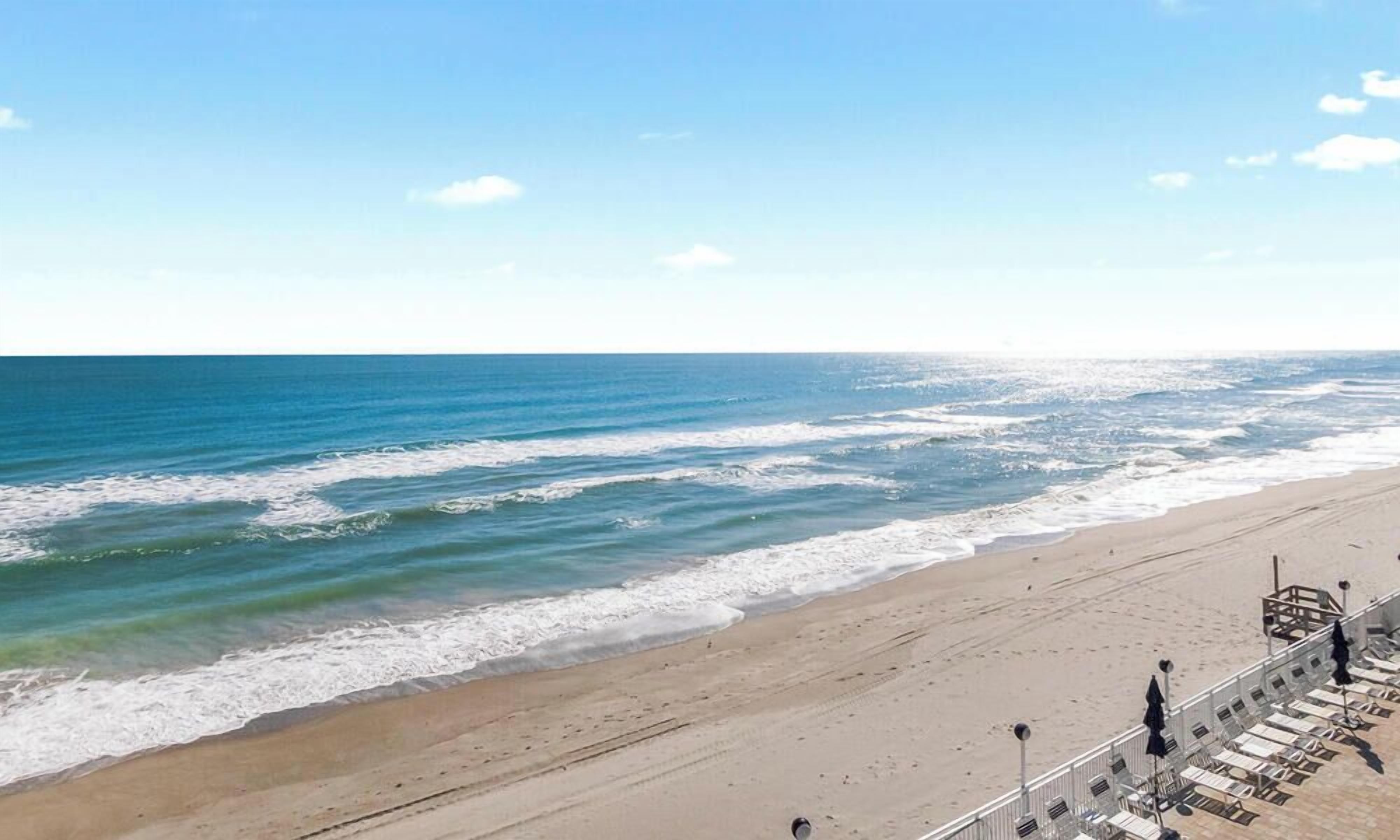 A beach with a promenade, sun loungers, and a clear view of the ocean.