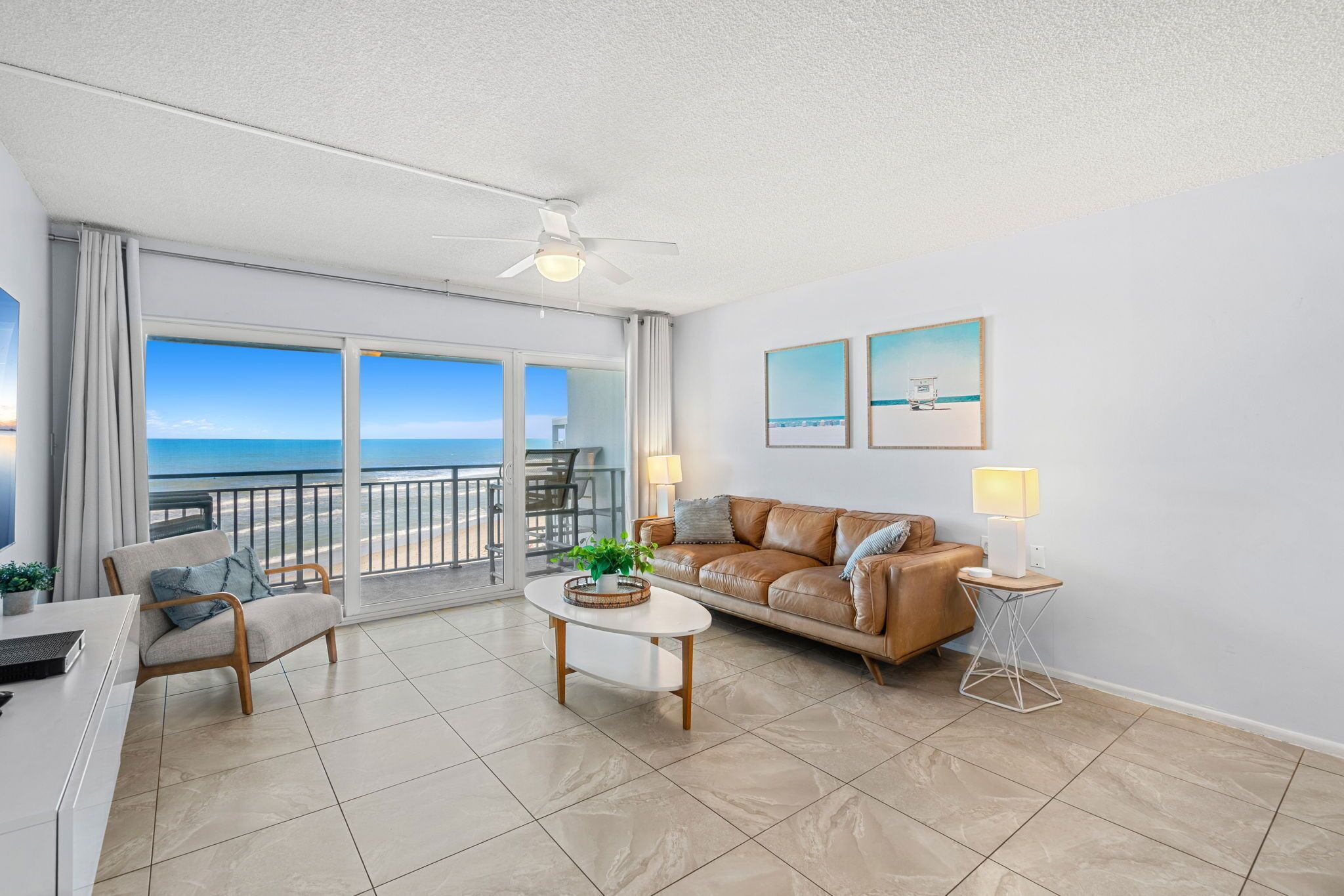 A spacious living room with a view of the ocean, a leather sofa, a coffee table, and a ceiling fan.