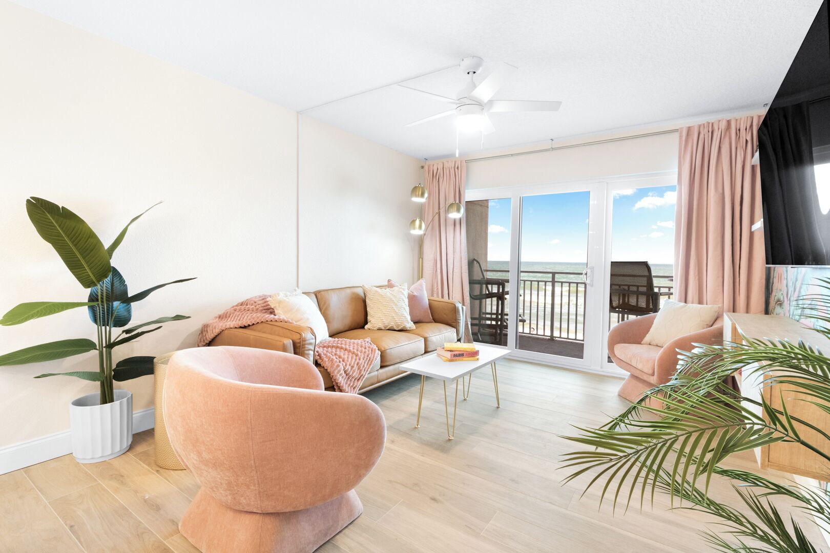Een ruime woonkamer met een bank, fauteuils en een salontafel. Er is een balkon met uitzicht op de oceaan.