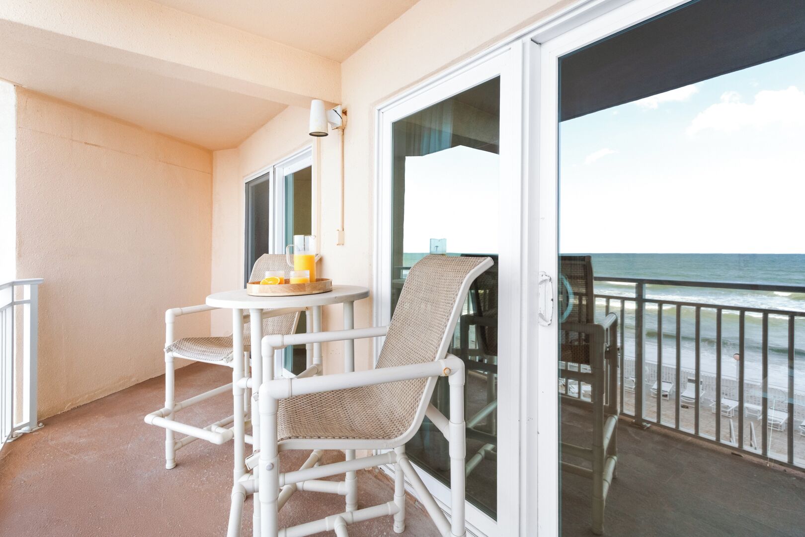 Un balcon avec une table, des chaises et une porte vitrée donnant sur la plage.