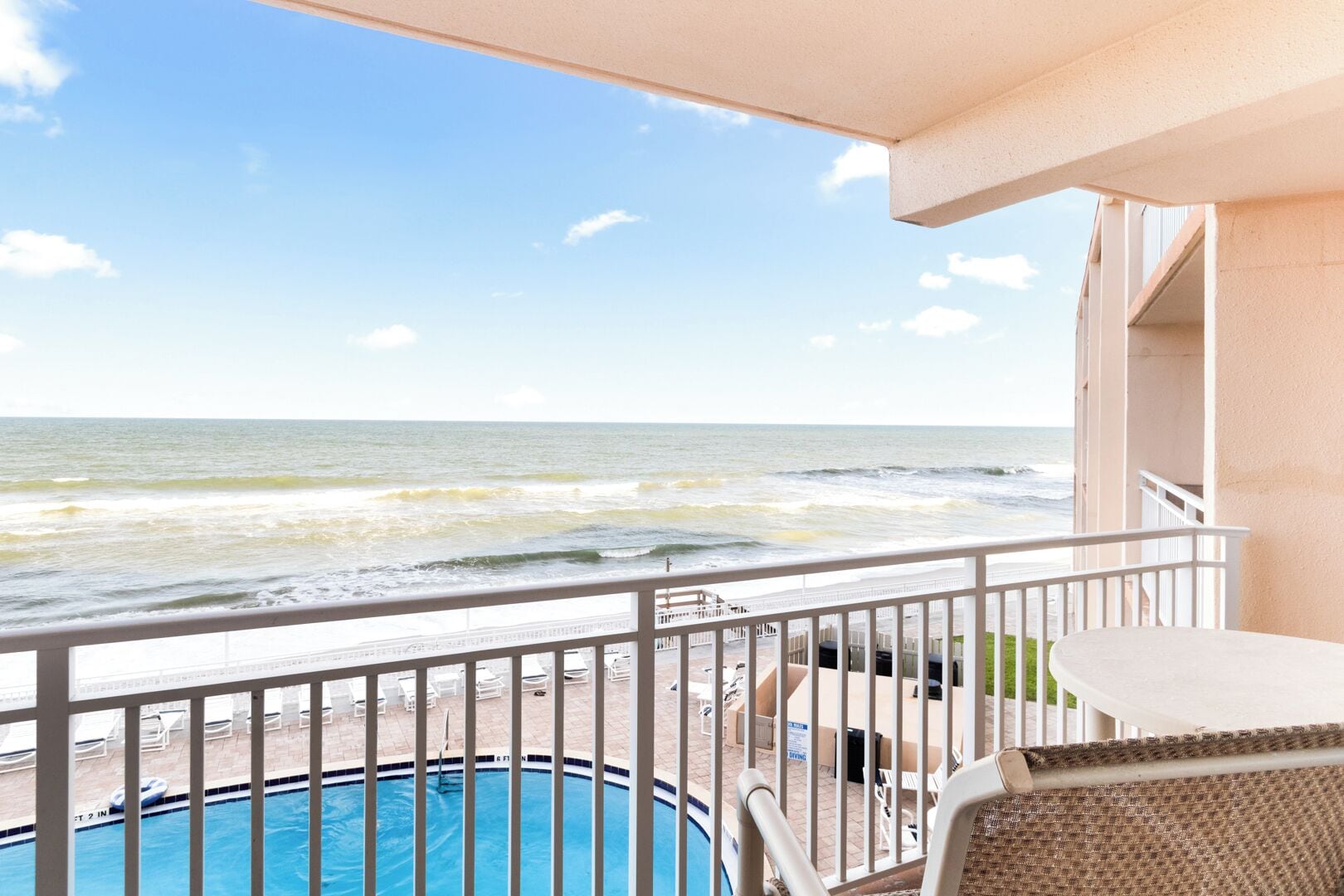A balcony with a view of the ocean, a pool, and outdoor seating.