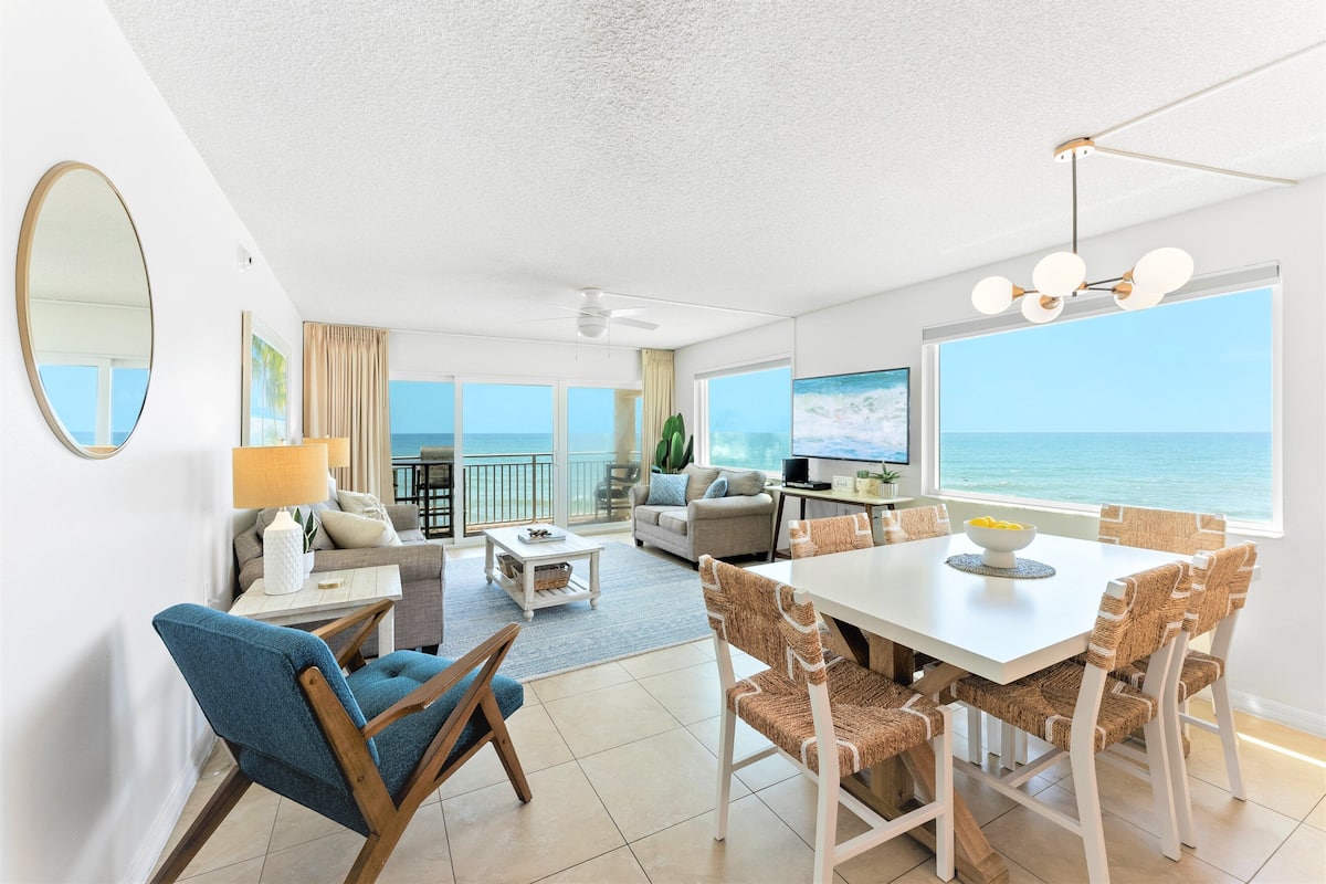 A modern living room with a dining area, large windows, and a view of the ocean.