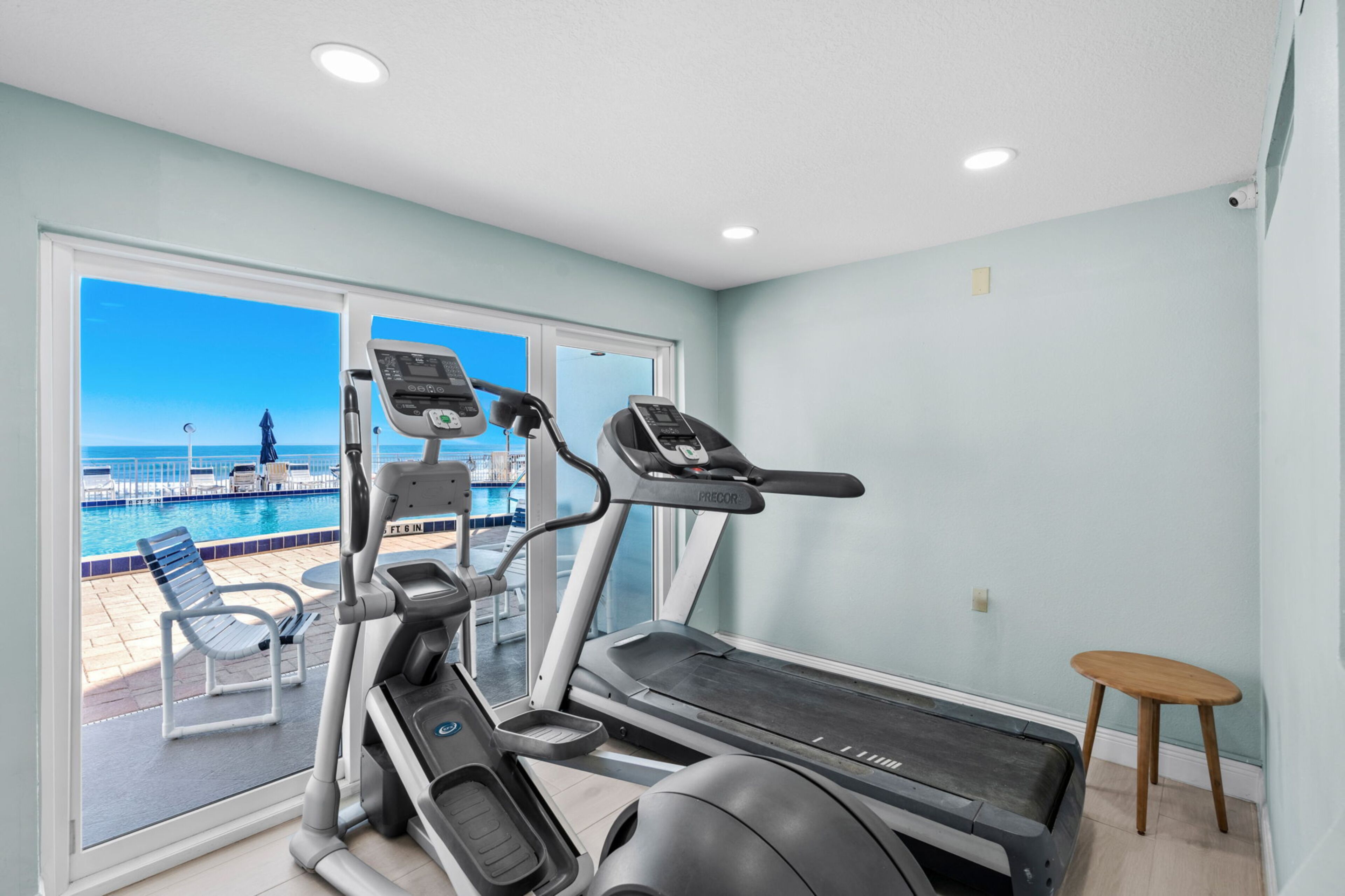 Une salle de sport équipée de tapis de course, avec vue sur une piscine et une plage.