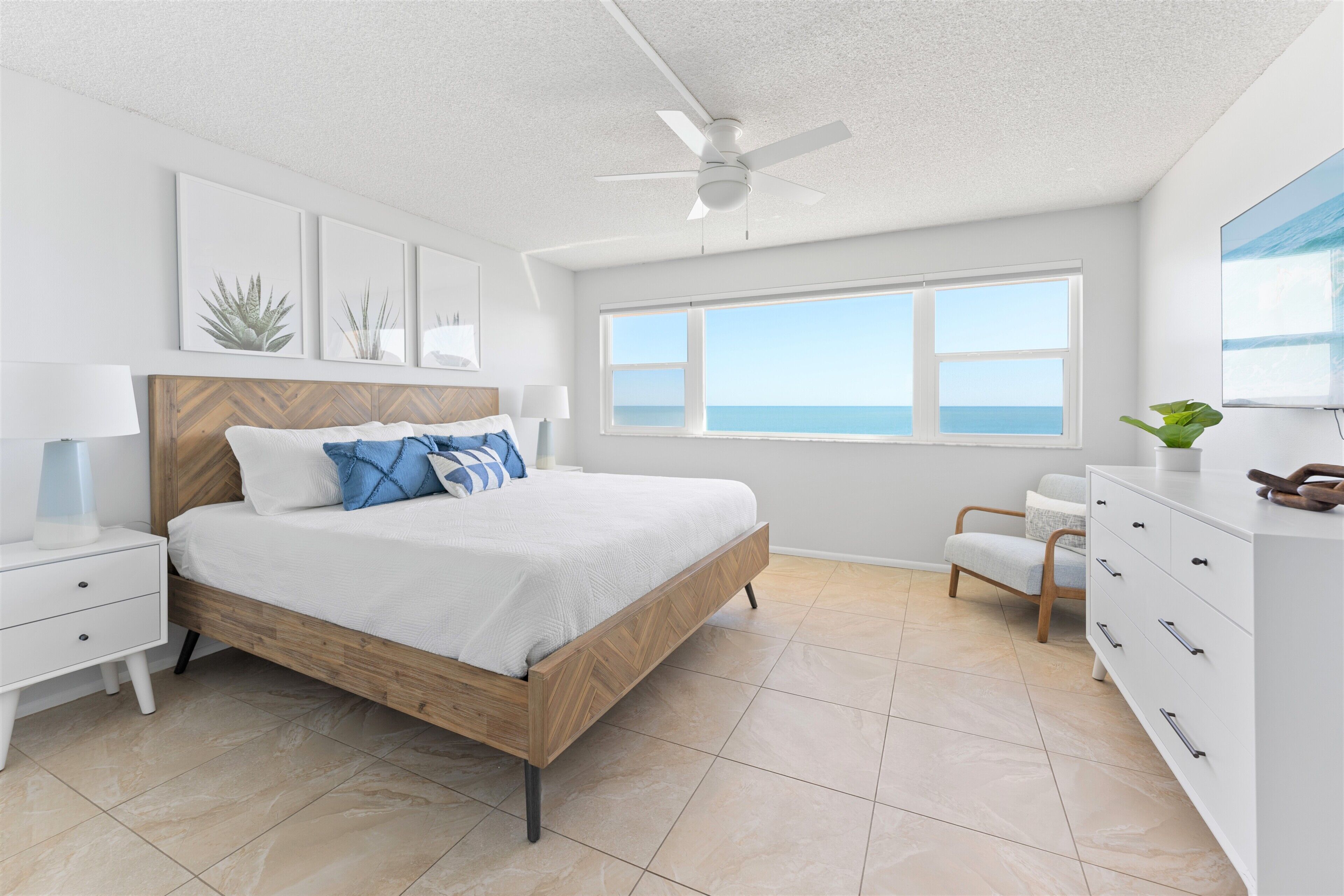 A bedroom with a bed, bedside tables, a ceiling fan, a window with a view, a dresser, and a chair.