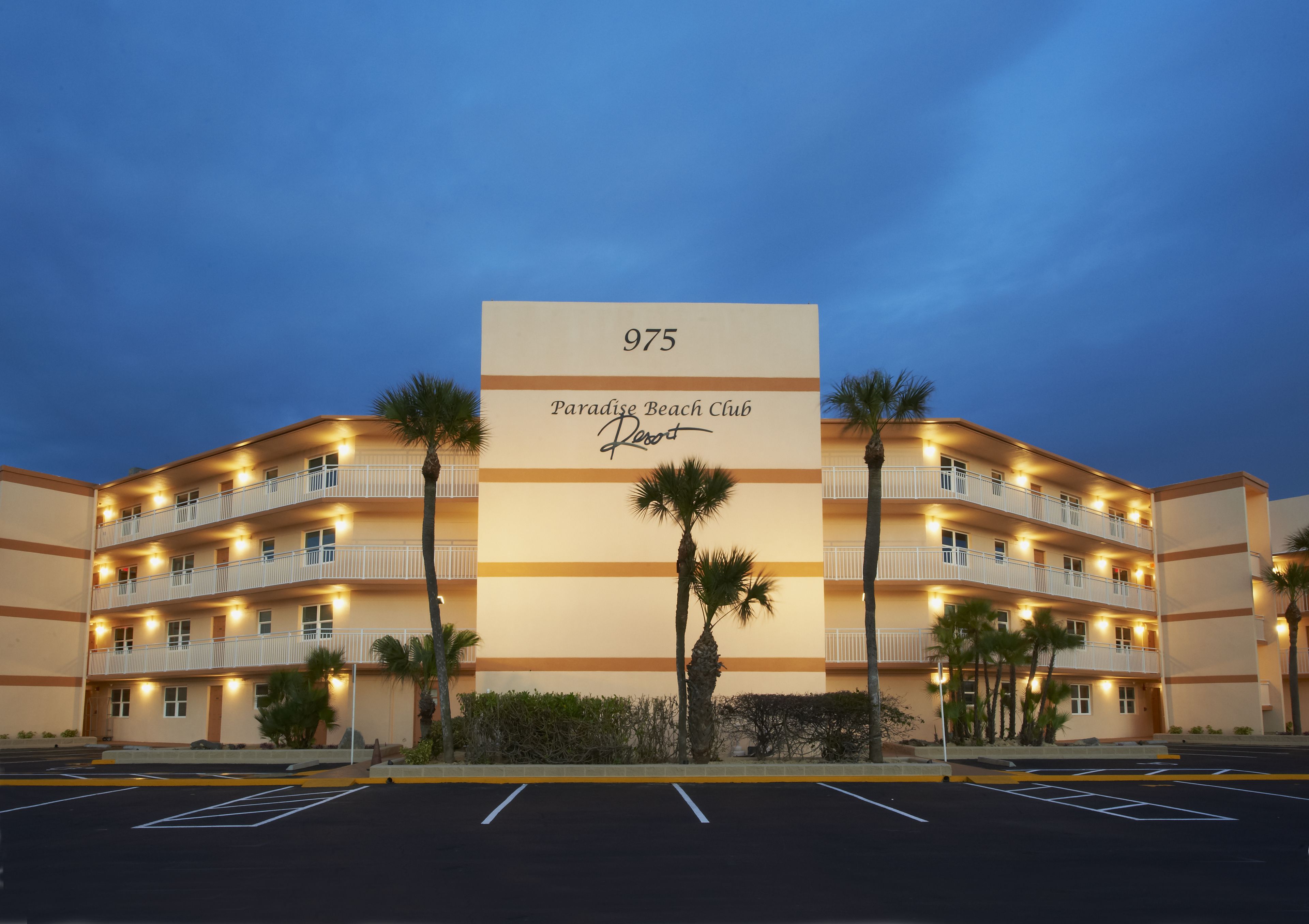 Ein mehrstöckiges Hotel mit einer großen Schilderanzeige der Nummer 975 und dem Namen "Paradise Beach Club Resort".