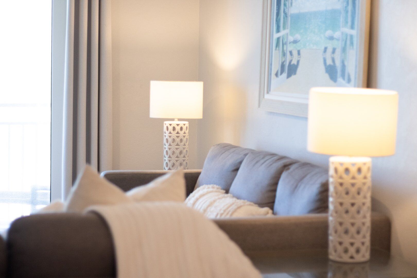 A modern living room with a grey sofa, two patterned floor lamps, and a framed picture on the wall.