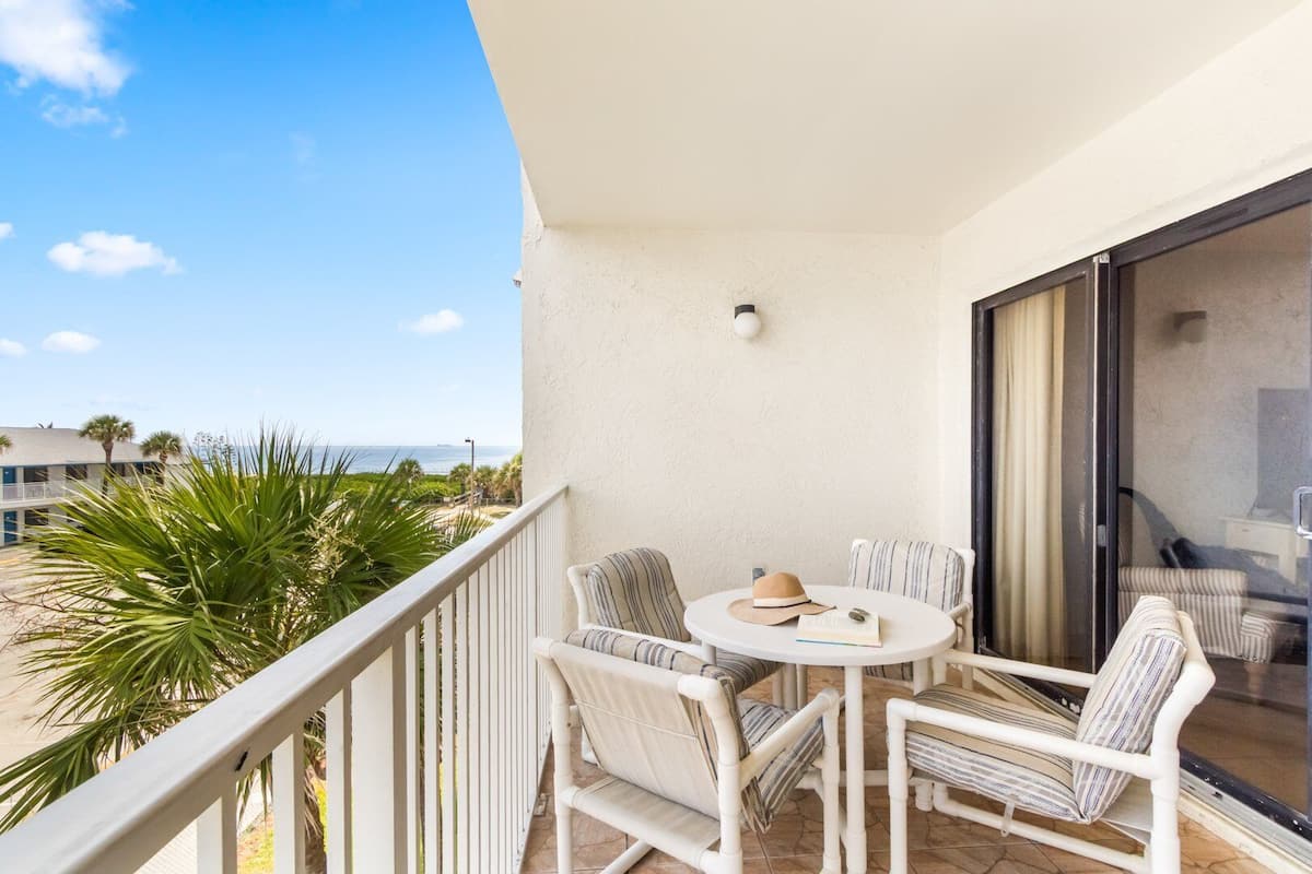 A balcony with a table and chairs, a hat, and an open door leading to a room.