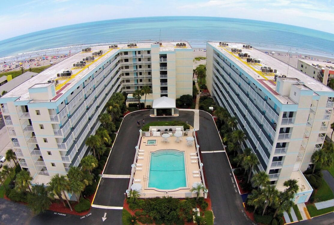A hotel with a central swimming pool, multiple floors, and a view of the beach.
