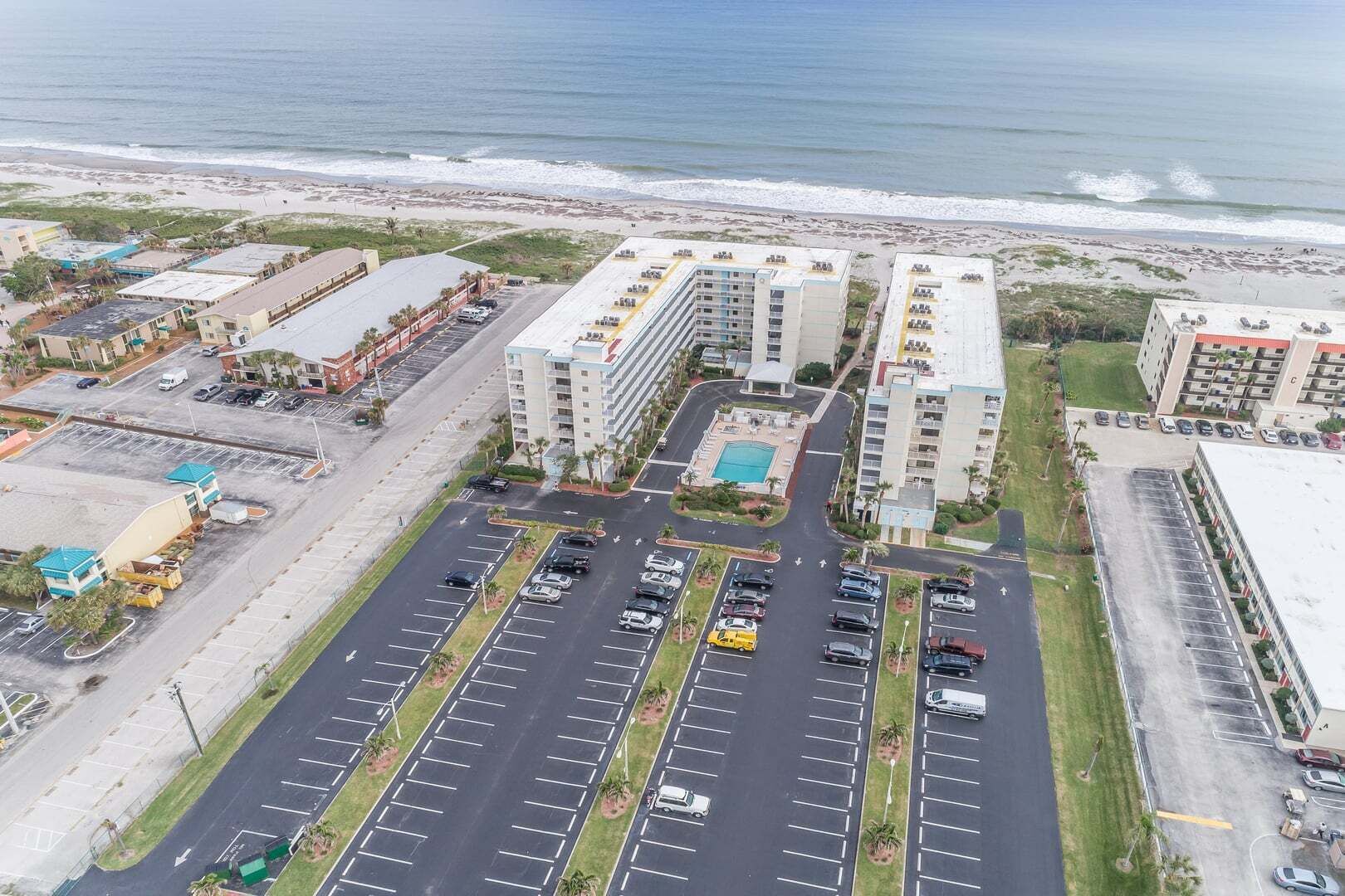 Ett hotell vid kusten med flera byggnader, en parkeringsplats och utsikt över stranden.