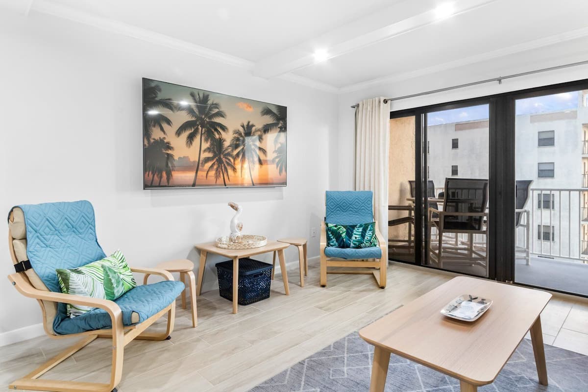 A modern living room with two blue armchairs, a wooden coffee table, and a painting of palm trees.