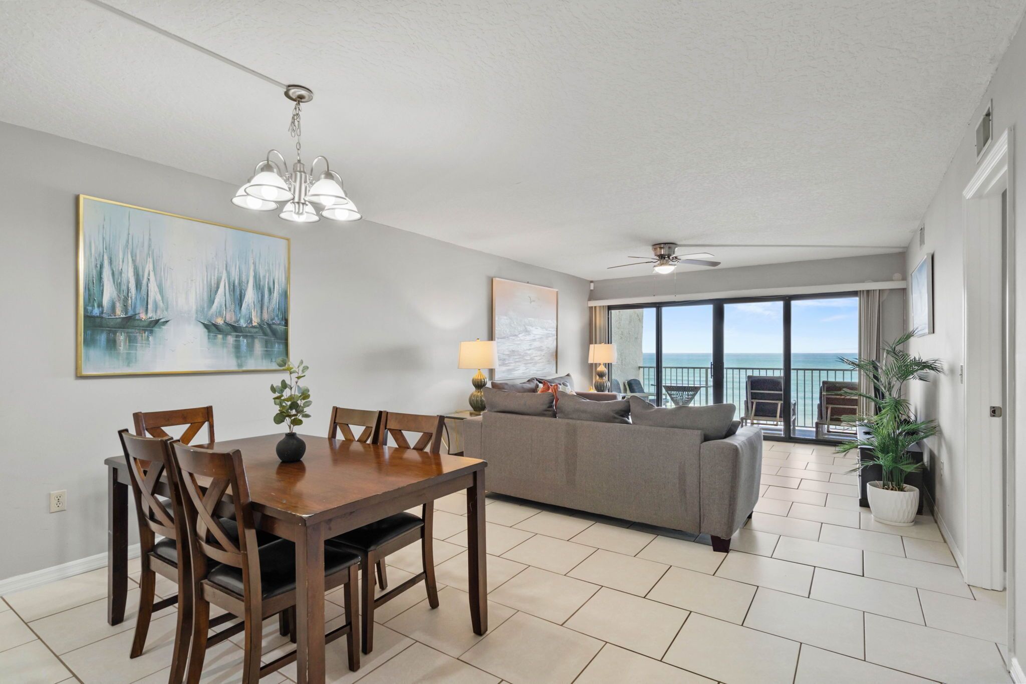 A spacious living room with a dining area, a large window with a view, a ceiling fan, and a painting on the wall.