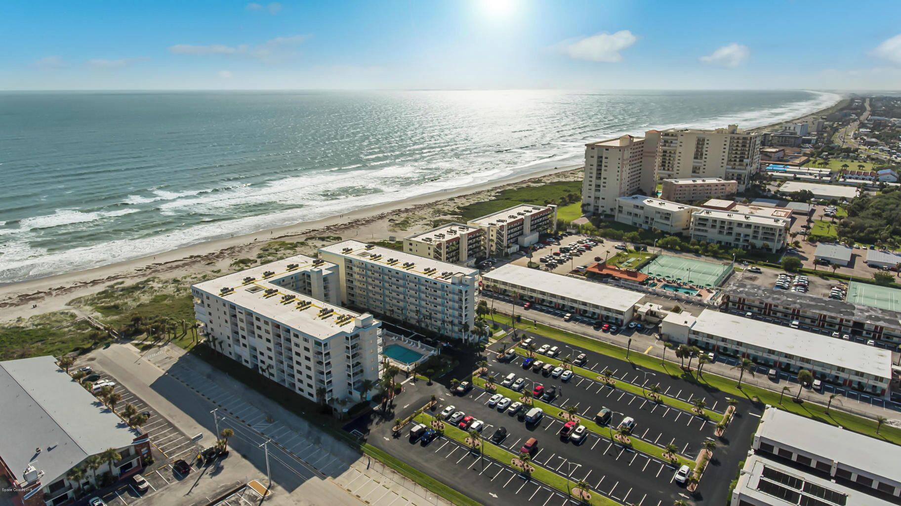 A coastal hotel with multiple buildings, parking lots, and a beach view.